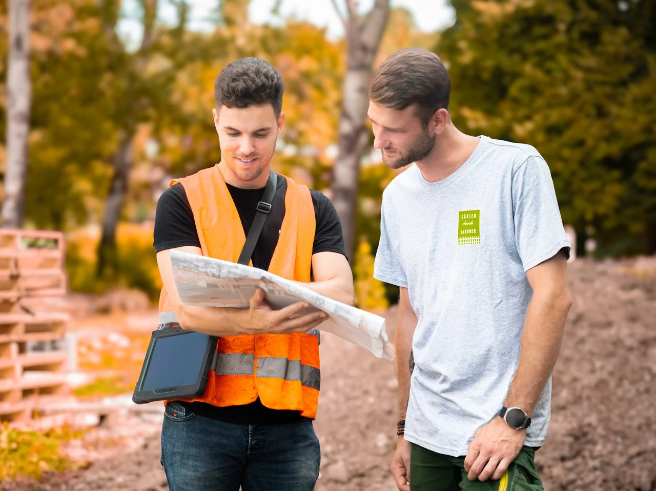 Zwei Menschen besprechen einen Gartenplan auf einer Baustelle im Garten- und Landschaftsbau.